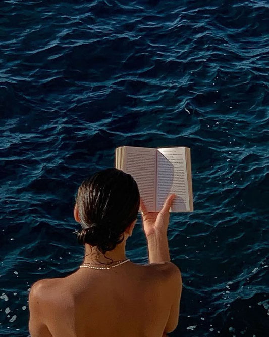 Jeune femme de dos, lisant un livre face à la mer. 