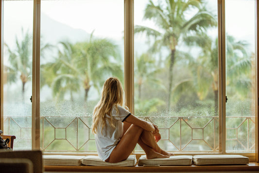 Jeune femme de dos qui regardent la nature à travers de grandes baies vitrées. Le paysage est une jungle d'Asie du sud